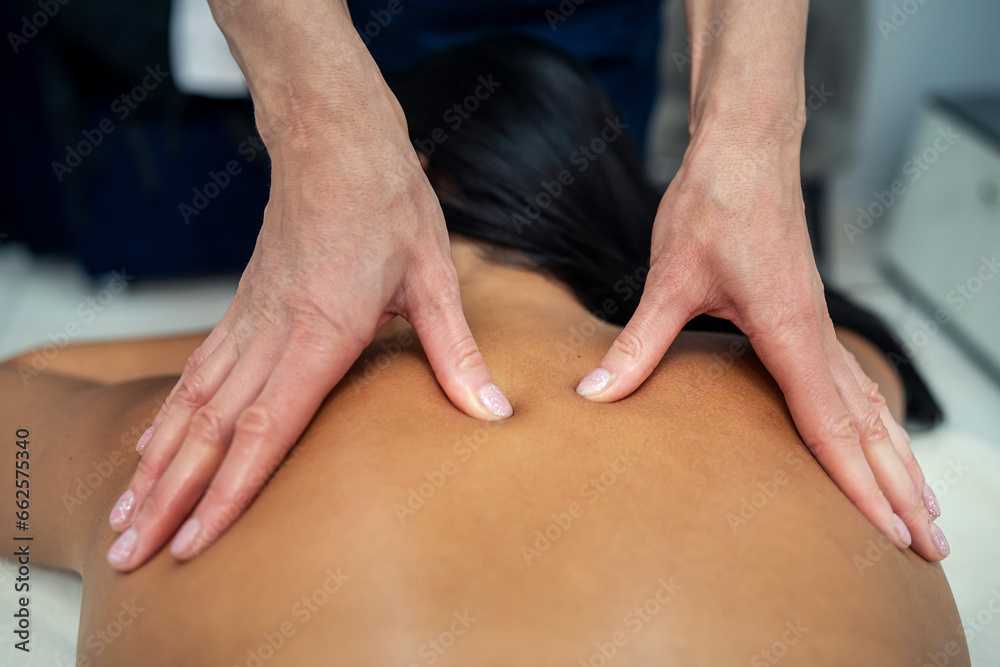 Attractive girl is relaxing on classic massage procedure in spa. Manual therapy. Masseur is doing back massage